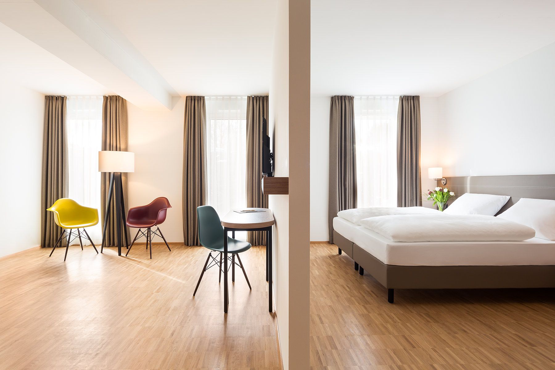 helles und geräumiges Hotelzimmer mit Raumteiler, Doppelbett und bunten Stühlen