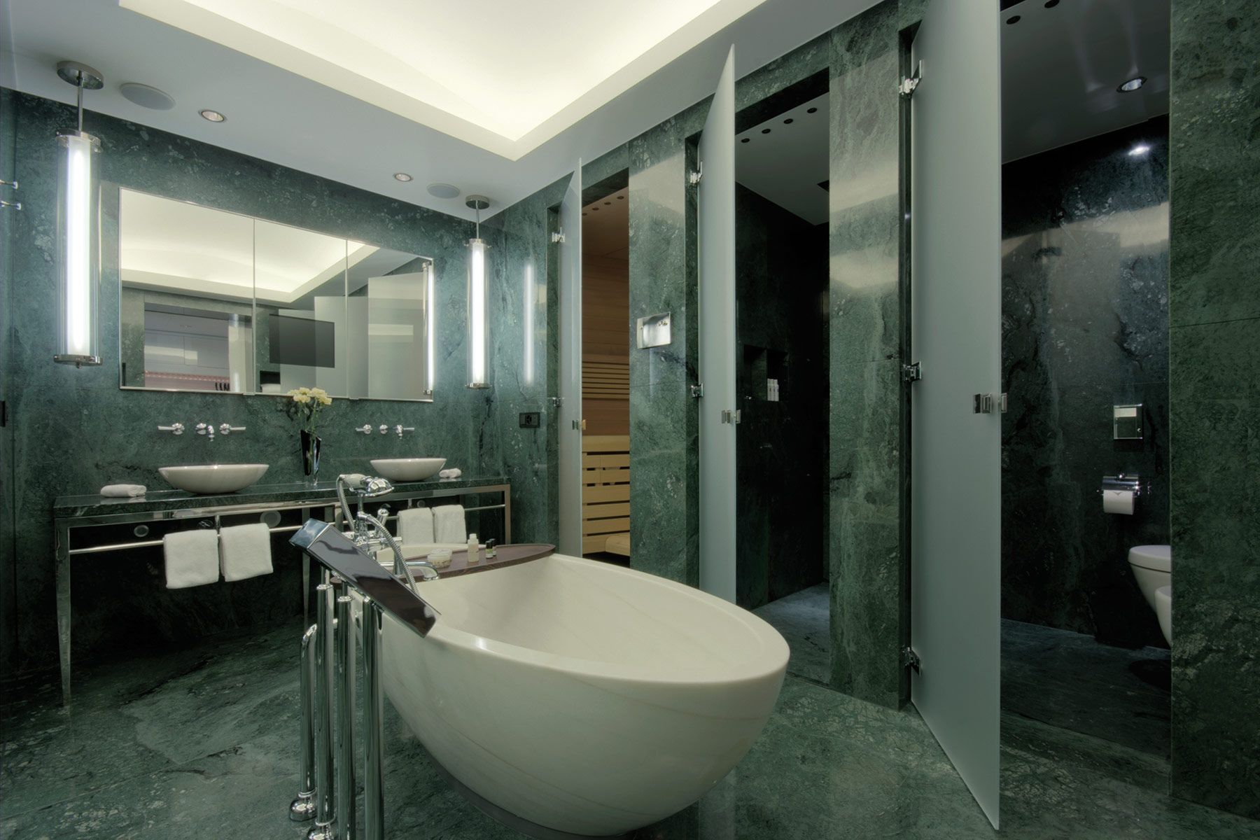 Badezimmer mit Steinoptik in Wand und Boden sowie freistehender Badewanne und einem großen Waschtisch