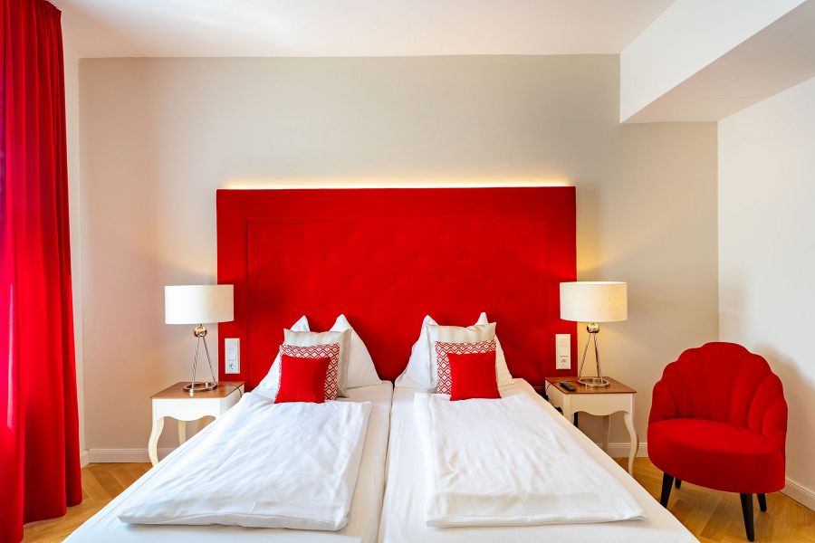 Hotelzimmer mit Doppelbett, rotem Sessel und antiken Beistelltischen