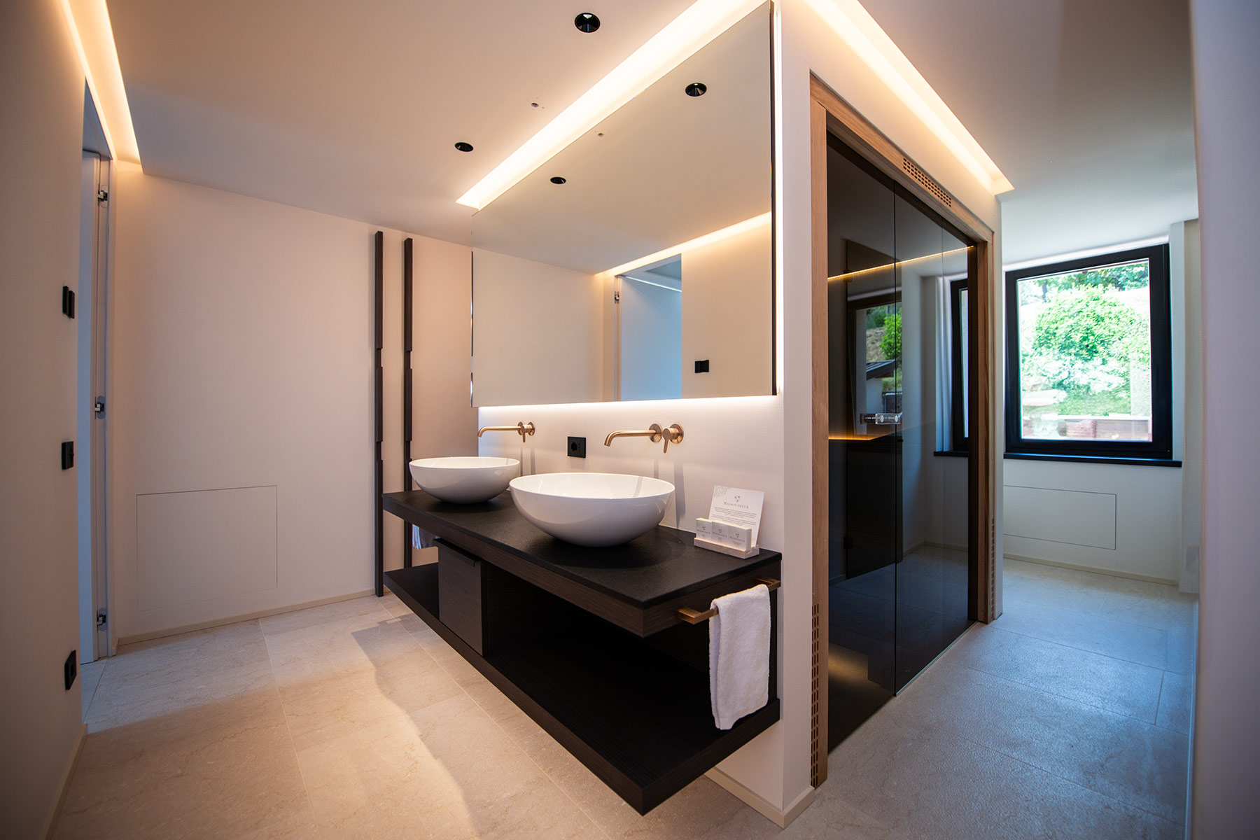 Modernes Spa-Ambiente im Appia Projekt Gargnano durch die Kombination aus edlen Kupfer-Armaturen fließenden Lichtlinien an der Decke und einem freien Blick in den angrenzenden Wellnessbereich