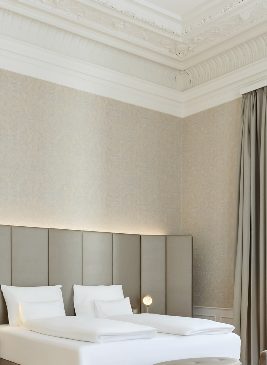 Detailansicht eines Doppelbetts mit Fokus auf die vertikale Struktur des grauen Textil-Kopfteils und die weiße Hotelbettwäsche