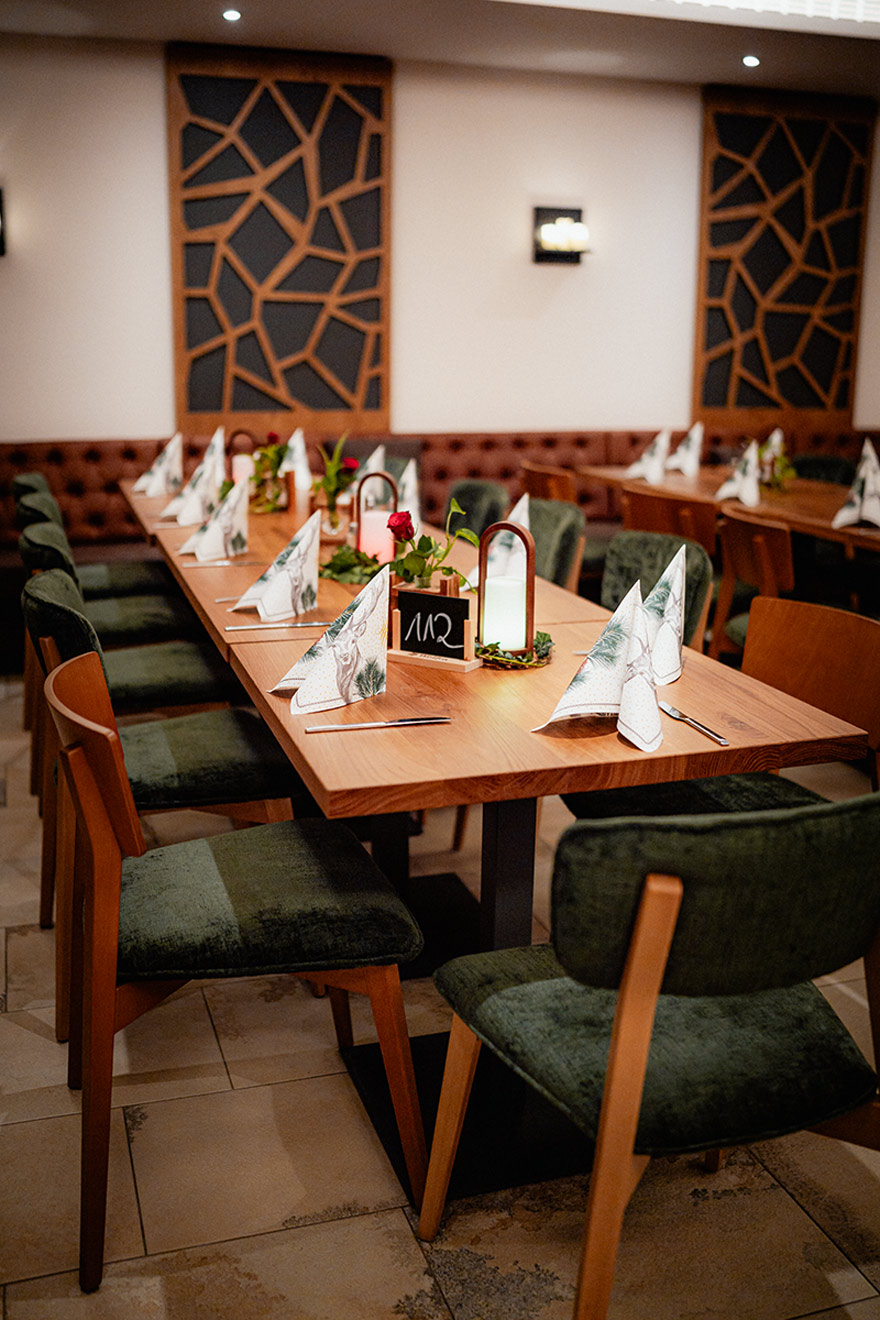 Gedeckter Tisch im Saal mit dekorativen Servietten, Blumen, Kerzen und umstehenden Stühlen im Gasthof Hummel.