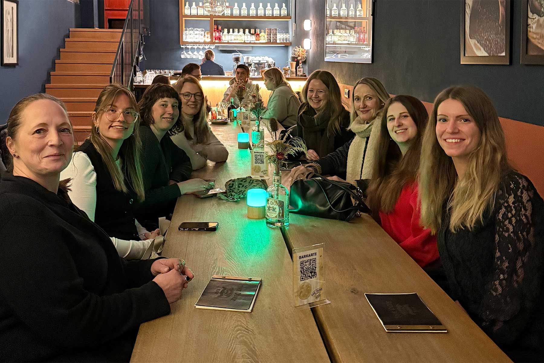 Appia-Team im Abendessen im Restaurant des Gasthofs Schäfflerwirt in Aschheim mit langer Holztafel gedimmter Beleuchtung und Barbereich im Hintergrund