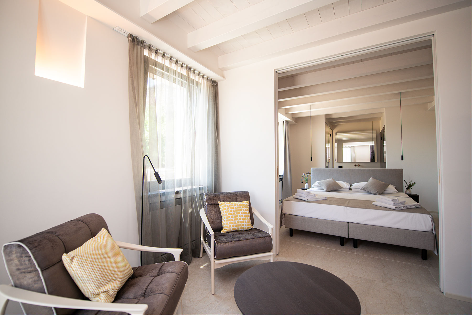 Ein einladendes Doppelbett mit gepolstertem Kopfteil in Grau und stilvoll arrangierten Kissen sorgt für maximalen Komfort im Schlafzimmer des Maison Selva Superior De Luxe Apartments