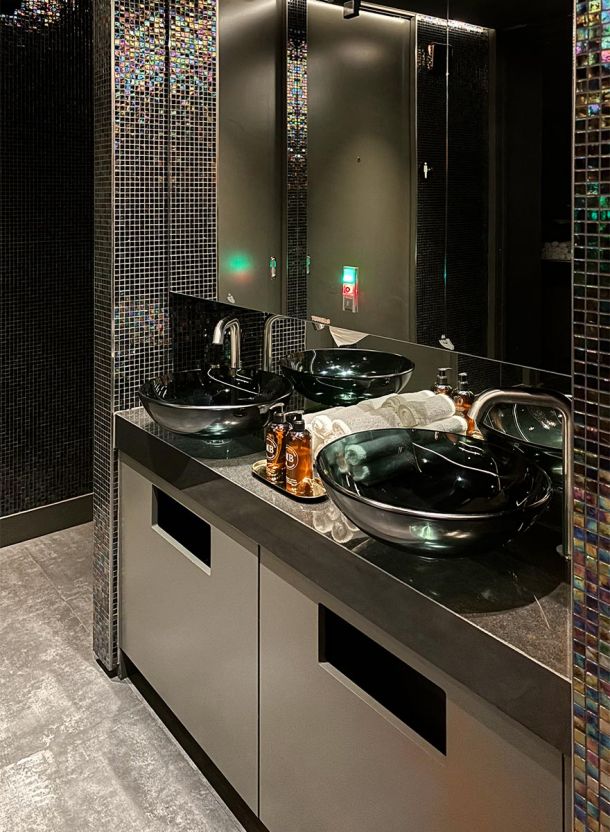 Hotelbad mit zwei aufgesetzten Glaswaschschalen dunklem Steinwaschtisch vertikalem Glasmosaik und großflächigem Wandspiegel