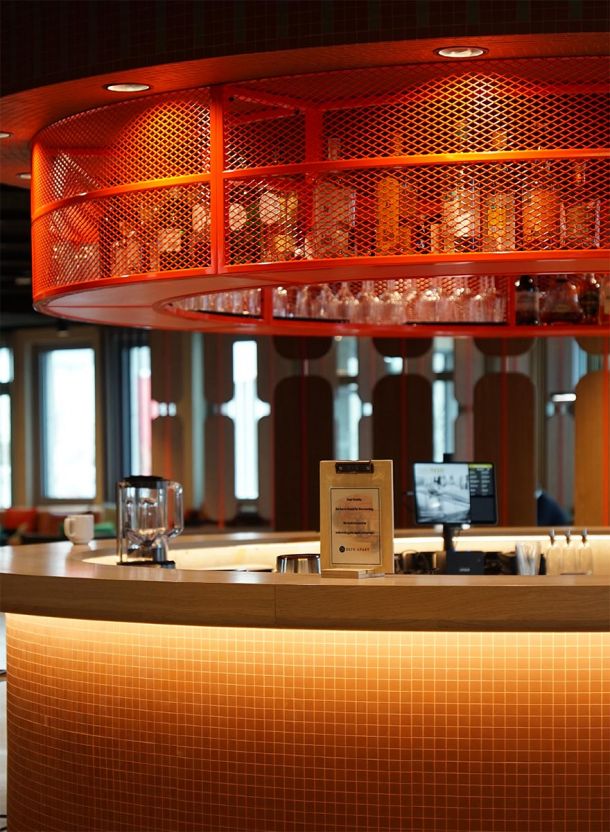 Empfangstresen im DEIN APART Unterföhring mit gerundetem Tresenkörper aus hellem Mosaik und warmer indirekter Beleuchtung