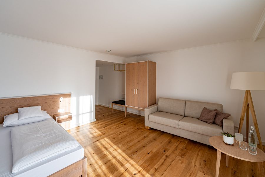 Einzelzimmer mit Couch, Stehlampe und Schrank im Hotel Schattenhofer