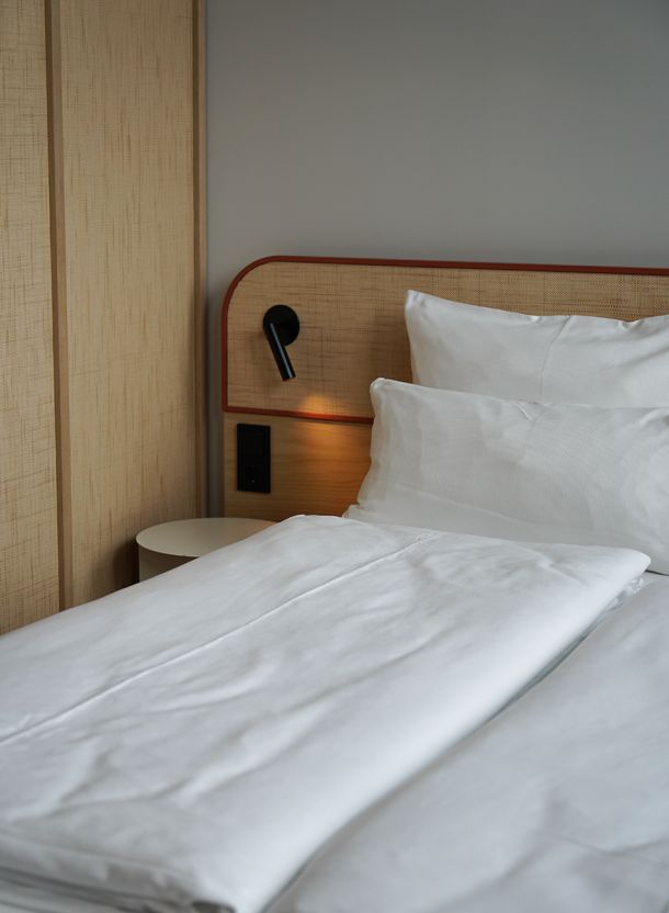 Detail aus dem Zimmer im DEIN APART Unterföhring mit klar gegliedertem Bettkopfteil in hellem Stoff schwarzer Leseleuchte