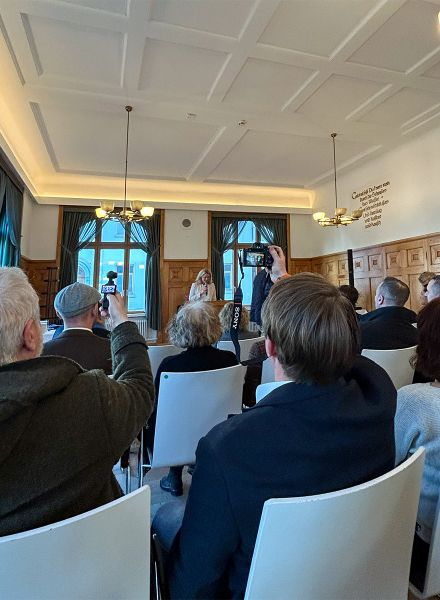 Eine Person hält eine Rede in einem Innenraum des Parkhotel Biberach. Mehrere Anwesende hören zu, einige machen Fotos.