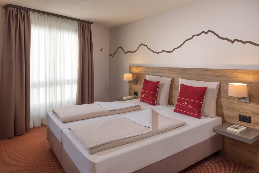 Doppelbett mit roten Dekokissen im Dorint Blüemlisalp