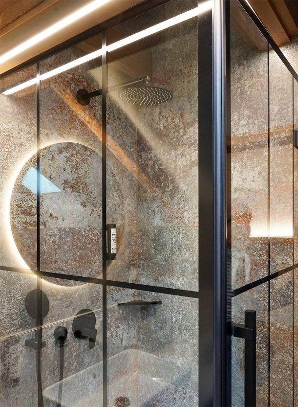 Badezimmer im Gasthof Schäfflerwirt Aschheim mit bodengleicher Dusche schwarzer Lofttür aus Stahlglas großformatiger Fliese und Holzdecke