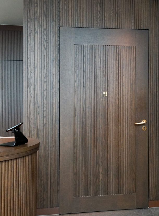 Holzlamellen Wand mit integrierter Tür im Hotelzimmer mit vertikaler Struktur Holzoberfläche Messinggriff ruhiger Farbgebung und klarer Linienführung