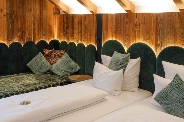 Doppelzimmer im Gasthof Schäfflerwirt Aschheim mit gepolstertem Bettkopfteil in dunklem Grünton integrierter Sitzbank Holzwand und sichtbaren Deckenbalken