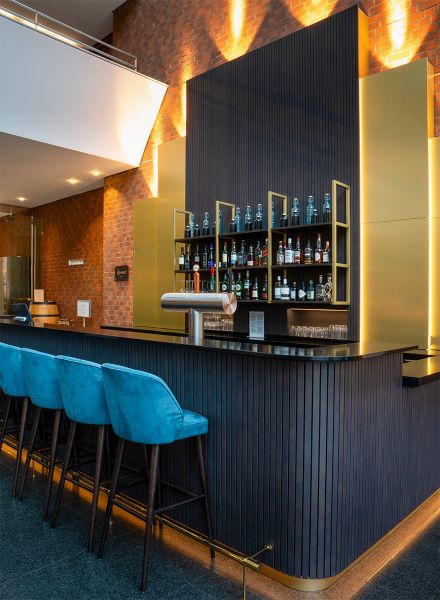 Hotelbar mit goldschimmernder Rückwand, Flaschenregal und akzentuierter Beleuchtung