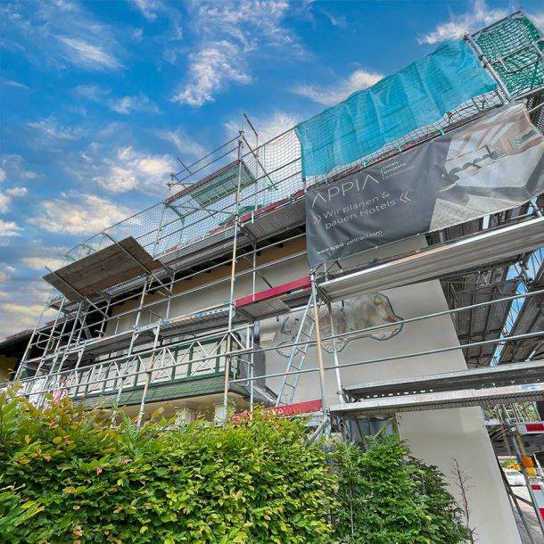 Fassade der Pension Schäfflerwirt in Aschheim mit Gerüst und Baustellenbanner Appia während der Bau- und Malerarbeiten