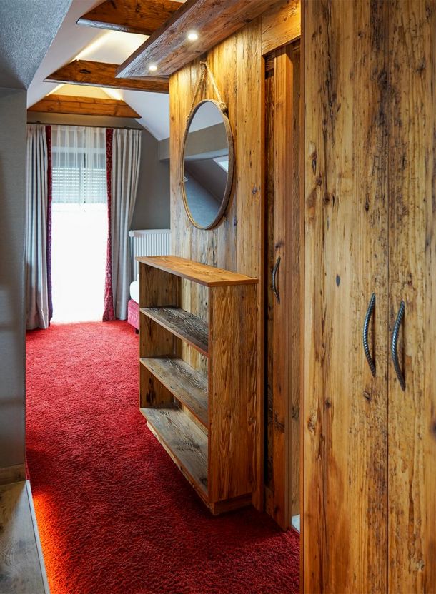 Rustikal gestalteter Zimmerbereich im Schäfflerwirt Aschheim mit naturbelassenen Holzelementen Deckenbalken offenem Stauraum und traditionellem Materialkonzept