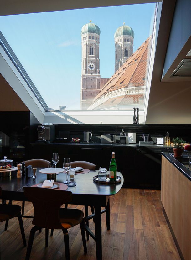 Essplatz im Do & Co Hotel am Marienplatz mit modern gedecktem Tisch integrierter Küchenzeile großzügigem Dachfenster und freier Sicht auf die Kirche und die historische Dachlandschaft Münchens