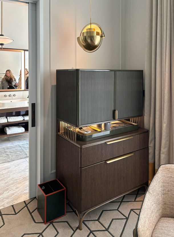 Schrank und Buffet im Rosewood Hotelzimmer München mit geriffelter Holzfront integrierter Ablage und goldfarbener Pendelleuchte darüber