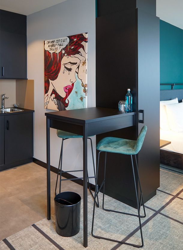 Apartmentzimmer im Dorint Hotel Garching mit schwarzem Stehtisch grünem Barhocker Leinwand mit grafischem Motiv und kompakter Küchenzeile