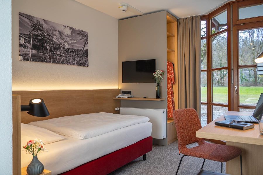 Einzelzimmer in warmen Farbtönen mit viel Tageslicht und Blick ins Grüne