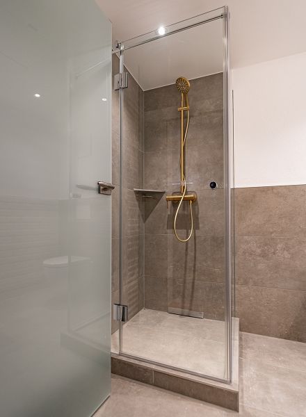 Dusche mit braunen Fliesen und goldenem Duschkopf 