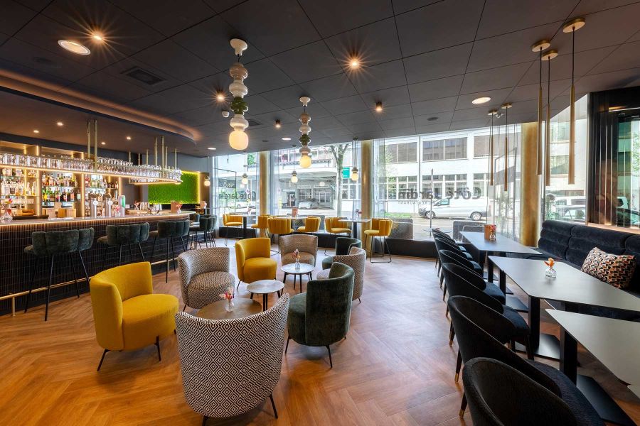 Großzügige Bar Lounge mit Sitzmöbeln Tischen und durchgehender Fensterfront sowie offener Raumstruktur