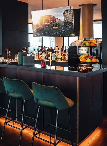 Hotelbar mit dunkler Theke und grünen Barhockern