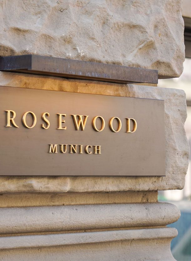 Goldene Rosewood Beschilderung auf grob behauener Natursteinmauer mit rechteckiger Metalltafel erhabenen Lettern und klarer Kantenführung