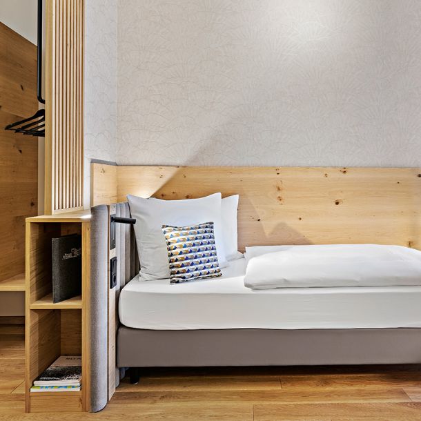 Einzelbett mit einem hölzernen Kopfteil, das in einem ruhigen Raum positioniert ist und Komfort und Entspannung betont