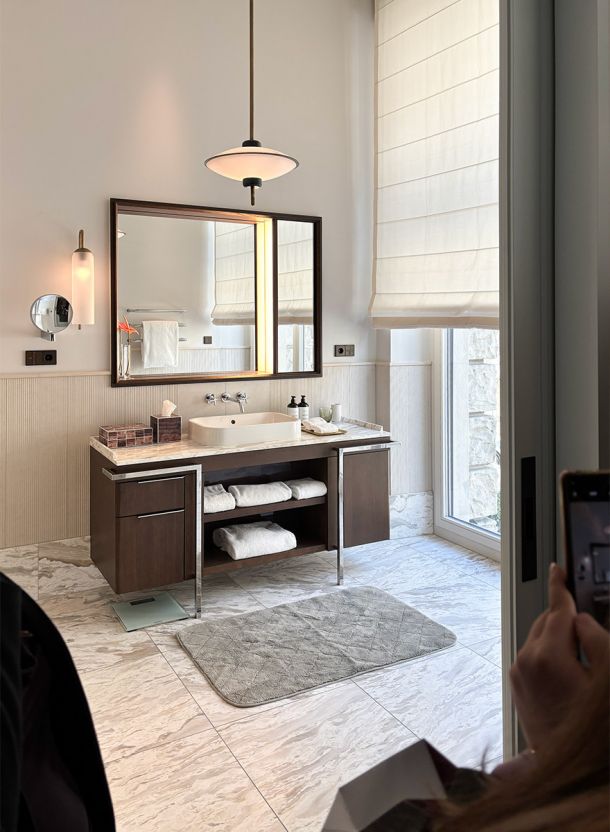 Bad im Rosewood Hotelzimmer in München mit modernem Waschtisch aus Holz großem Spiegel Wandbeleuchtung und hellem Natursteinboden