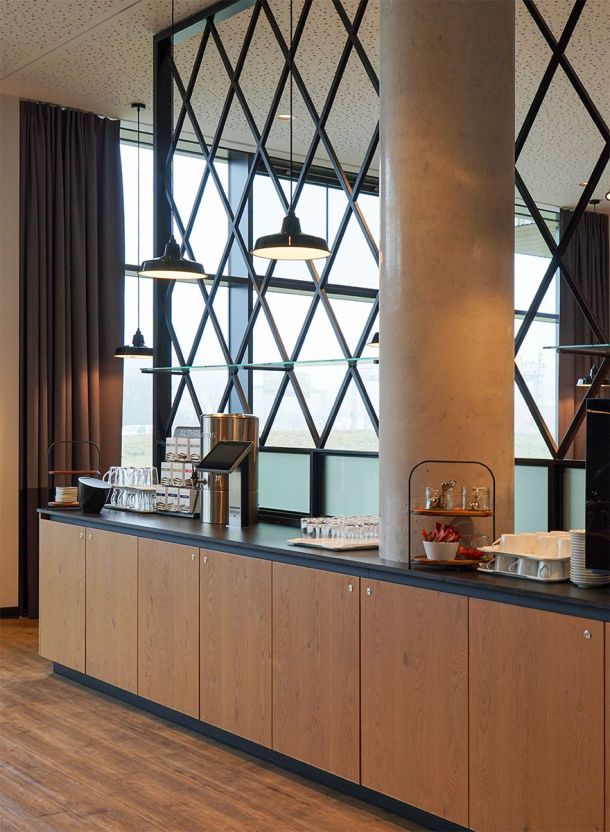 Langer Buffetbereich mit durchgehender Holzmöblierung dunkler Abstellfläche Pendelleuchten und strukturierendem Säulenelement im Vordergrund